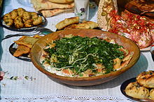 Tajik kurutob in a large shallow wooden bowl, surrounded by other, more dumpling-like Tajik dishes.