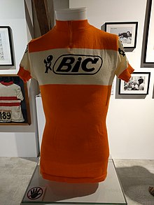 Photographie d'un buste avec maillot orange dessus, un logo et une inscription BIC figurent sur fond blanc sur la poitrine