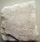 "Batu kecil, kira-kira berbentuk persegi dan berwarna abu-abu muda, bertuliskan naskah hieroglif dari masa firaun Kerajaan Lama Mesir Pepi II"