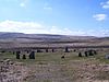 Circle of standing stones on pastureland, against a background of purplish hills and a blue sky with white clouds