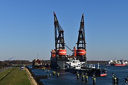 総トン数82,000の石油タンカーとその奥に控えたSSCVスレイプニルの写真。ブームを高く掲げた10,000トン起重機がタンデムで聳え立っており、スレイプニルの巨大さが際立っている。ロッテルダム港にて2020年撮影。