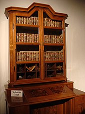 Une armoire vitée contenant des volumes de bois semblables à des livres.