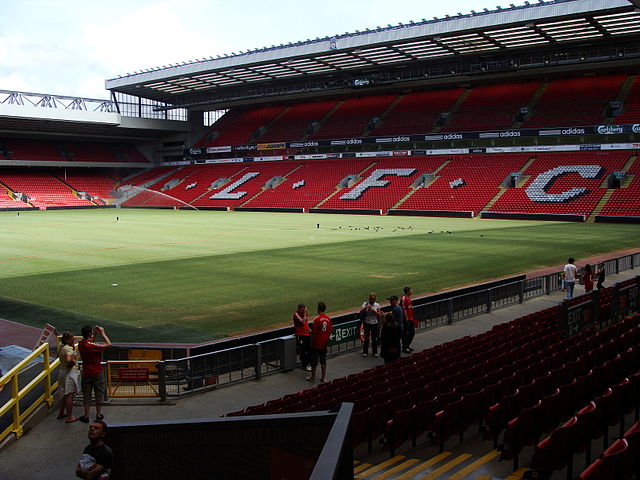 A two-tiered stand which has red seats, there are also white seats which spell out "L.F.C. In front of the stand is a field of grass