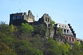 Fotografia de um castelo parcialmente em ruínas localizado no topo de uma colina arborizada.