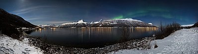 A wide view over Storfjorden (a part of Lyngen fjord) in a winter night with some Aurora borealis running across the sky.