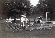 Фотография двух человек, перепрыгивающих через барьер.  Левый барьер опрокинут.