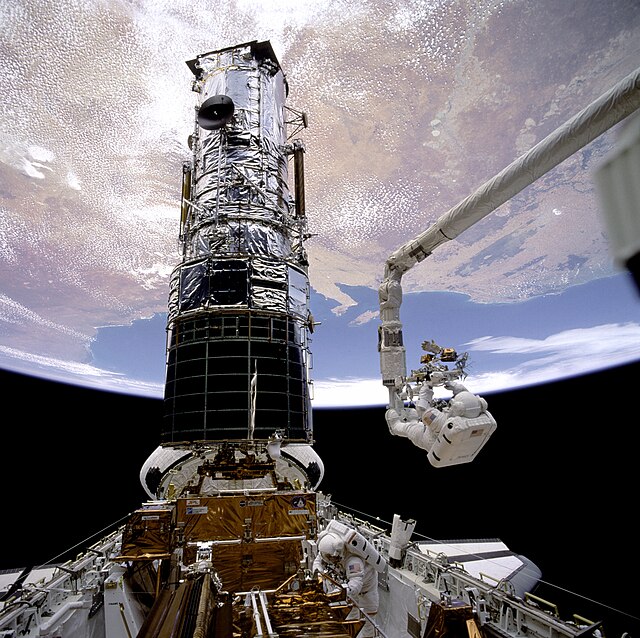 Story Musgrave, anchored on the end of the Canadarm, prepares to be elevated to the top of the Hubble Space Telescope during STS-61.