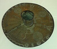 Tobillera realizada de una barra de latón macizo del tipo que usan las mujeres Igbo. Ahora en la colección de Wolverhampton Art Gallery. El tubo de la pierna se extiende unos 7 cm a cada lado del disco de 35 cm.[3]​[4]​