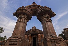 in front of the Jagamohana is a masterpiece dating from about 900 AD. It is a detached portal consisting of two pillars supporting an arch within a semicircular shaped pediment. The decoration of the arch, with languorously reclining females and bands of delicate scroll-work, is the most striking feature.