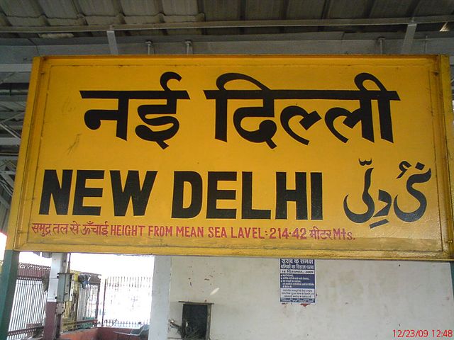 A multilingual New Delhi railway station board. The Urdu and Hindi texts both read as: naī dillī.