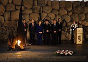 Секретарка у посети Израелу поново пали вечну ватру и полаже венац у Меморијалном центру сећања (Јад Вашем); на фотографији направљеној ноћу је још седам особа, од којих су две на Хилариној десној страни и две на њеној левој страни а за говорницом; у првом плану је венац, а у позадини зид од огромног камења (Јерусалим, 3. март 2009)