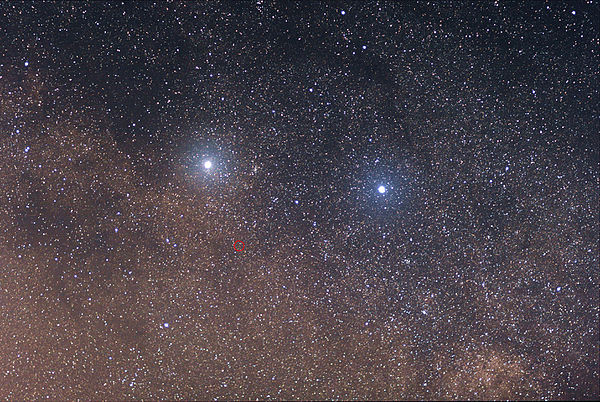 Two bright stars against a dense background of fainter stars, with one of the fainter stars circled in red