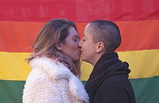 Couple kissing in front of rainbow flag (42328458024).jpg