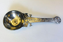 A spoon with an ornately decorated handle, two fish reinforce the junction of bowl and handle which ends in a flower like pommel