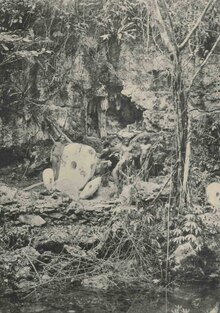 Foto em preto e branco de homens posando ao lado de moedas de pedra na frente de uma cintura