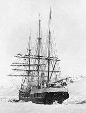 Rear view of a three-masted sailing ship with all sails furled, lying in an ice-covered sea