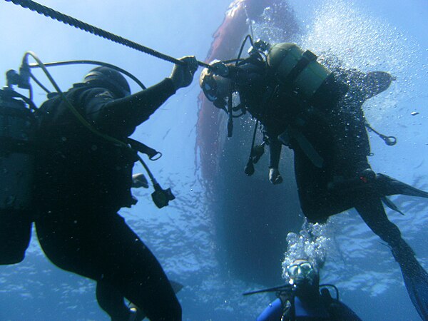 Divers using the anchor cable as an aid to depth control during a decompression stop during ascent.