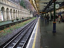 View along station platform with timber and glass canopy over supported on cast-iron columns. To the left a disused platform without track is visible