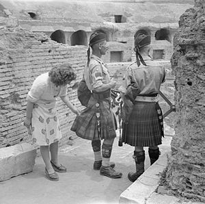 Le 6 juin 1944, à Rome où sont entrés depuis peu les Alliés, au Colisée, une femme italienne examine avec curiosité les kilts de deux cornemuseurs-majors.