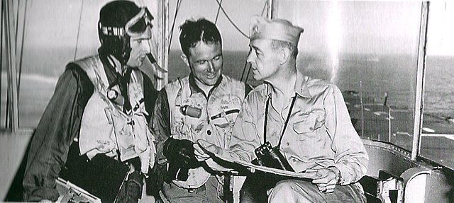 Captain John S. Thach (right) as commanding officer of the escort aircraft carrier USS Sicily (CVE-118) during the Korean War, discussing a mission wi