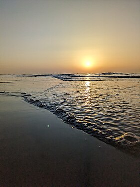 Welle mit Luftblasen am Strand vor einem Sonnenuntergang