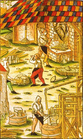 A hammer mill. In the background is the bloomery (Rennofen), in front of it a bloom is being coarsely freed of dross. In the near foreground, the bloom is being forged under the hammer. Agricola Hammerwerk mit Rennherd.jpg