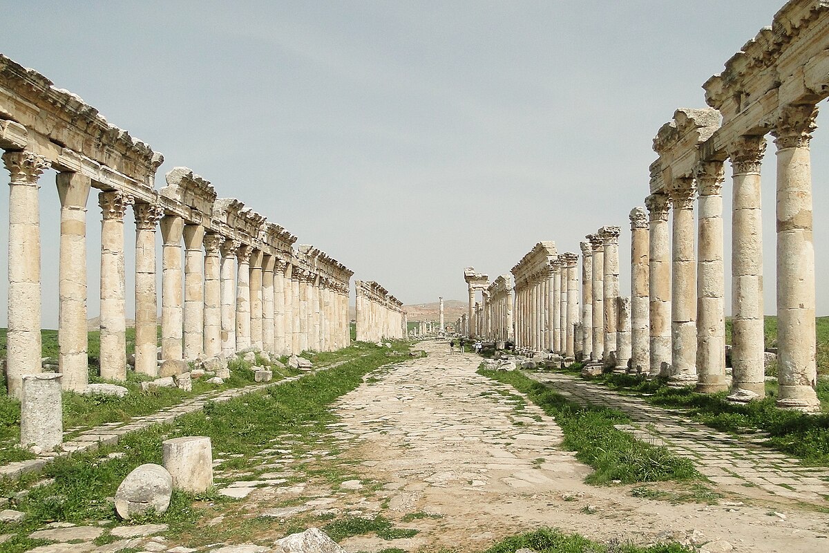 A view of road lined with columns， some of which are still topped with a decorative frieze