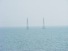 Two electrical transmission towers standing in a featureless expanse of water under a hazy sky