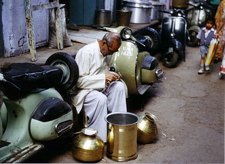 Street handicraft: here a skilled metalsmith in Agra, India sits between scooters in a commercial area making careful observations in the practice of his trade