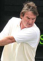 Ein braunhaariger Mann in einem weißen Hemd schwingt eine Zweihand-Rückhand