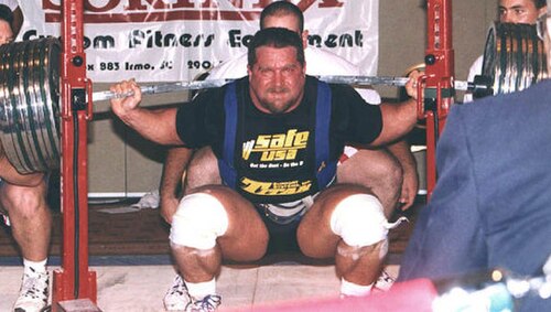 Kirk Karwoski completing a heavy squat in competition. Note the spotters either side of him and the power cage which the barbell was lifted out of.