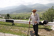 Elderly man with a beard and hat selling carrots on the side of a road