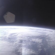 The edge of Earth, heavily overexposed, in the lower half of the image, with black space above. In between them, a blue haze layer from the atmosphere. There is a lens flare in one corner.