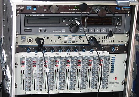 A 19-inch rack holding several professional audio devices including an 8x8 matrix mixer at the bottom, made by Midas Consoles. The matrix mixer has 8 vertical faders to control output level, 8 light gray potentiometers (rotating pots) for input level control, and 64 dark gray pots for matrix mixing. There are also 64 on/off buttons, one for each input/output intersection. Matrix mixer in rack.jpg