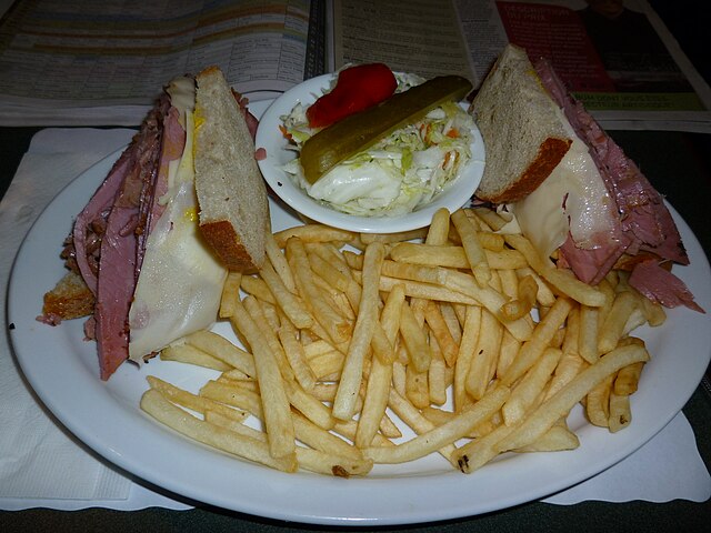 An atypical smoked meat sandwich topped with Swiss cheese, served with coleslaw, French fries and one quarter of a pickle. Generally, the authentic ve