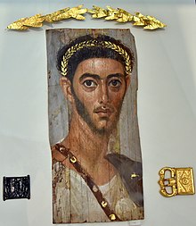 Encaustic painted mummy portrait of a Roman officer c. 130, with a blue sagum, silver fibula, white tunic, and red balteus, with related grave goods (Antikensammlung Berlin) Mummy portrait of a Roman soldier, c. 130 CE. From er-Rubayat, Fayum, Egypt, acquired in 1927 CE. Encaustic painting on wood. Altes Museum.jpg
