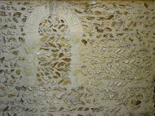 Muro di pietra disposto a spiga di grano con tracce di una vecchia finestra