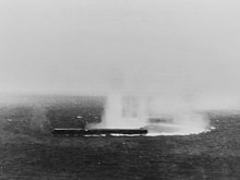 The Japanese aircraft carrier Shōkaku under attack by planes from USS Yorktown, during the morning of 8 May 1942. Splashes from dive bombers' near misses are visible off the ship's starboard side as she makes a sharp turn to the right.