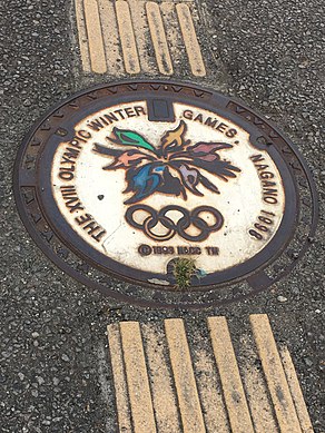 Stylized manhole cover displaying the Nagano Olympics emblem, with tactile paving