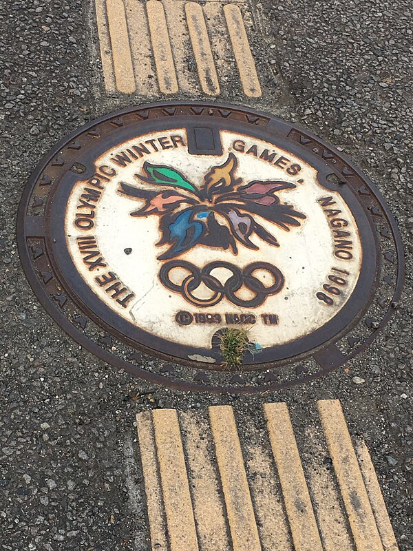 Stylized manhole cover displaying the Nagano Olympics emblem, with tactile paving