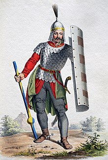 Muž s knírem v železné helmě, drátěné košili a šedých kalhotách. V jedné ruce drží žlutomodrý dřevec, ve druhé železný štít.