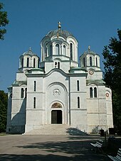 Barevná fotografie zobrazující kostel v orientálním stylu se třemi kopulemi a velmi bílými stěnami.