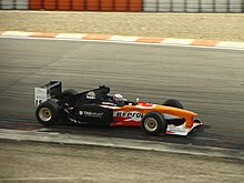 Foto af en F1-enkeltsæde, med den forreste orange og den bageste, sort.
