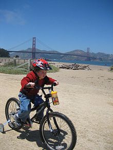 Boy on bicycle before the Golden Gate Bridge. Boy with helmet on training wheels.jpg
