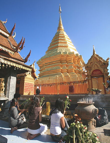 Worshippers making offerings of incense, flowers and candles to a chedi at Wat Doi Suthep, Chiang Mai, Thailand