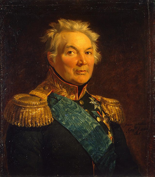 Painting shows a gray-haired man with a round face wearing a very dark military coat with gold epaulettes, a gold collar and a blue velvet sash over his shoulder.