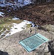 Uma grande pedra com um cartaz no centro, rodeada por um gramado coberto de neve.