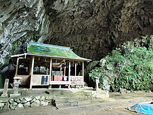 Farbfoto eines religiösen Holzgebäudes am Eingang zu einer Höhle.