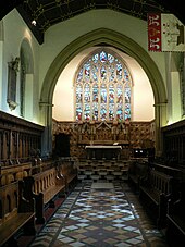 Photo de la chapelle ; La même chapelle avec l'arche du chœur plus large et un retable de pierre en dessous d'un grand vitrail. Un pavillon décoré d'un navire est accroché en haut de la paroi de droite