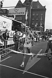 Photo of Gerard Nijboer running on the: street. And raising one hand as he reaches the——finish line ribbon